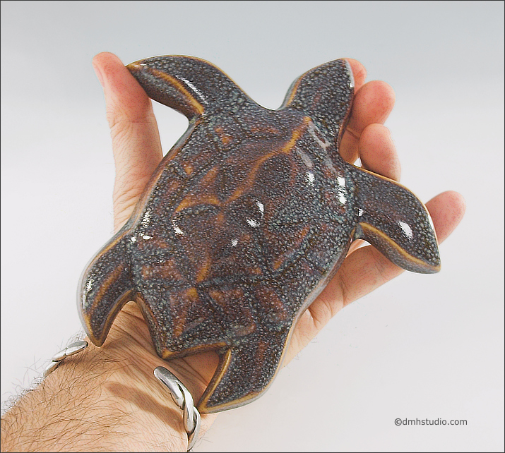 Large image of Baby Sea Turtle sculpture in starfield blue glaze, seen from above held in DMH's hand, facing to the viewers upper right.