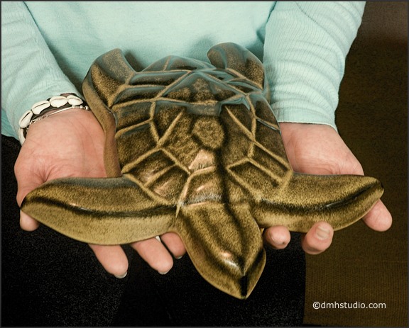Large image of Hanalei Sea Turtle sculpture in black gold glaze, being held by Mary K. Seen from slightly above, and facing out to the viewer.