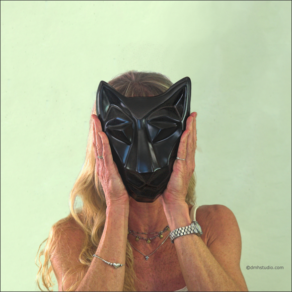 Large image of Mary K. holding sister cat mask in diamond black. Portrait facing the viewer.
